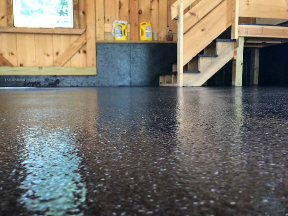 Low-angle view of a glossy dark Graniflex flake-coated garage floor in a wood-clad shop, with a small staircase visible in the back